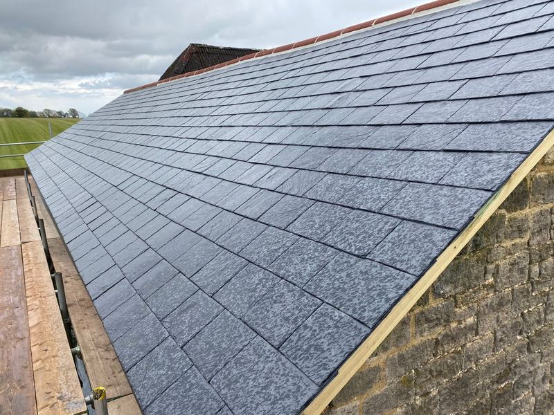 Newly laid natural slate roof with clay ridge tiles above a stone gable wall